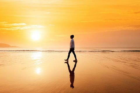 A person walks on the beach as the sun sets over the ocean.